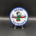 Patch featuring a cartoon character holding an airplane with 'NASWF T-6 TEXAN II' text on a black background Snoopy dog peanuts