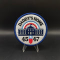 Patch with 'Daddy's Home' text and numbers on a stand against a dark background Trump Patch 45 47