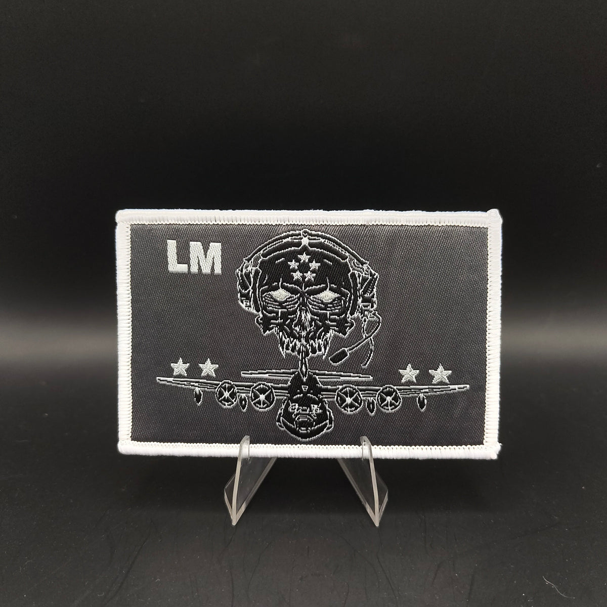 Black and white patch with skull design and 'LM' initials on a stand against a black background loadmaster aircrew kc-130j c-130 crew patch